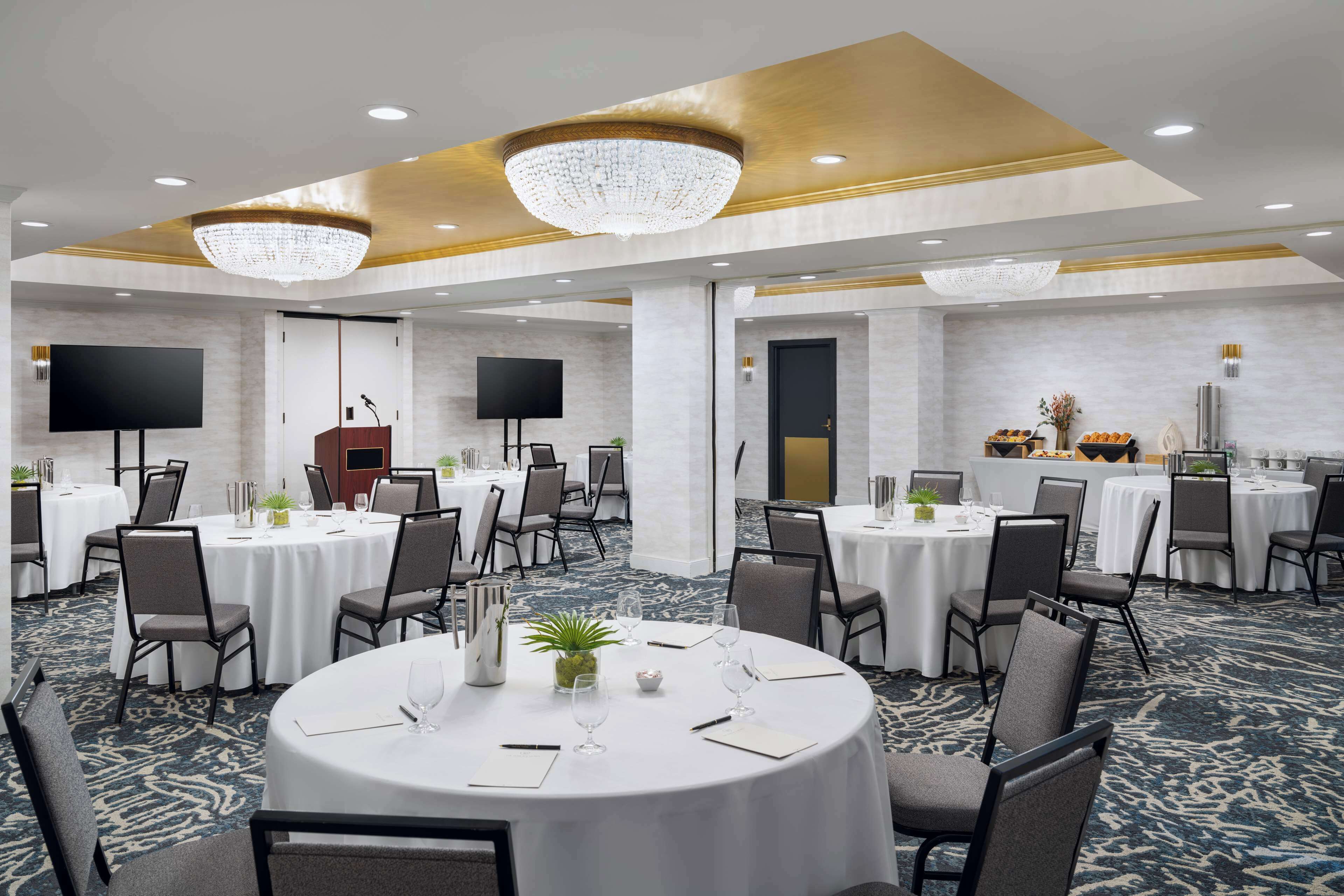 A conference room with round tables, chairs, a podium, and a large screen.