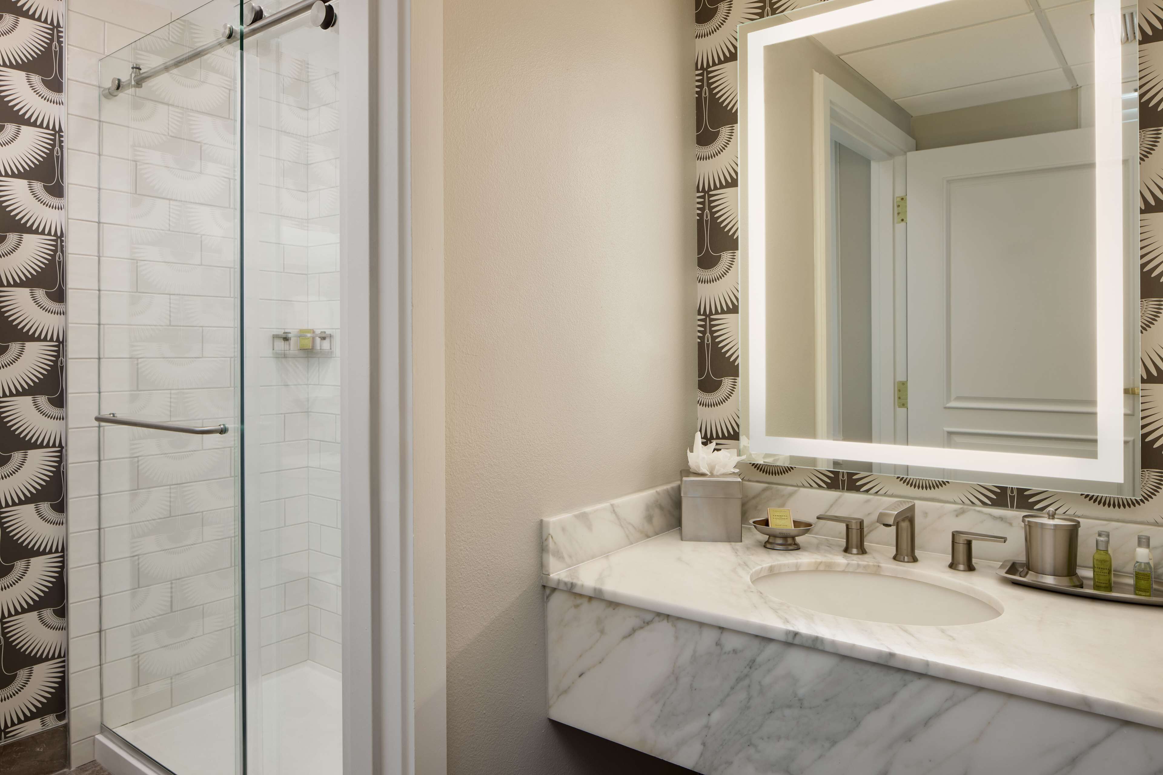 Un baño con cabina de ducha de vidrio, lavabo de mármol y un espejo grande.