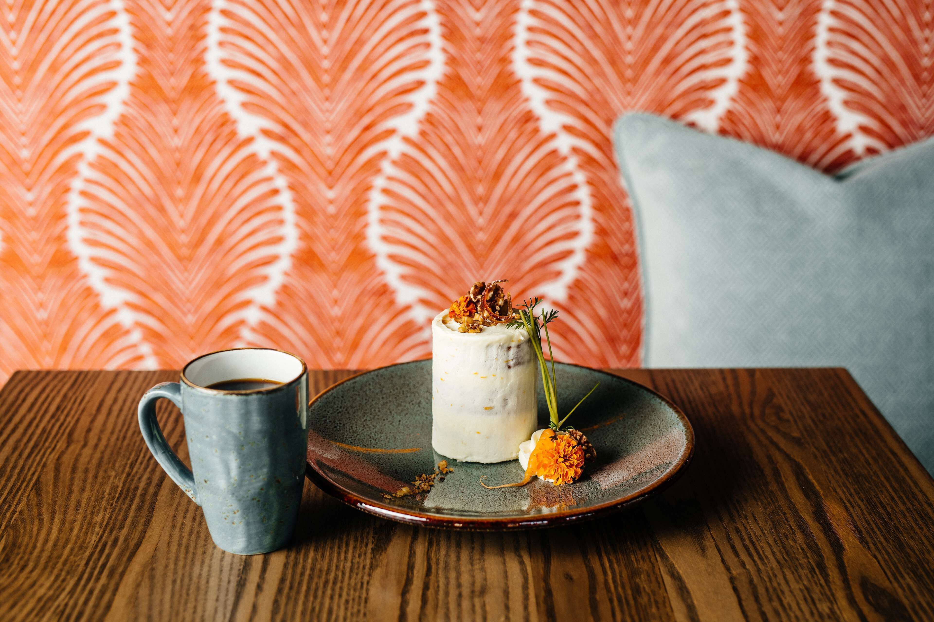 Un postre sobre un plato de cerámica con una taza de café en una mesa de madera.