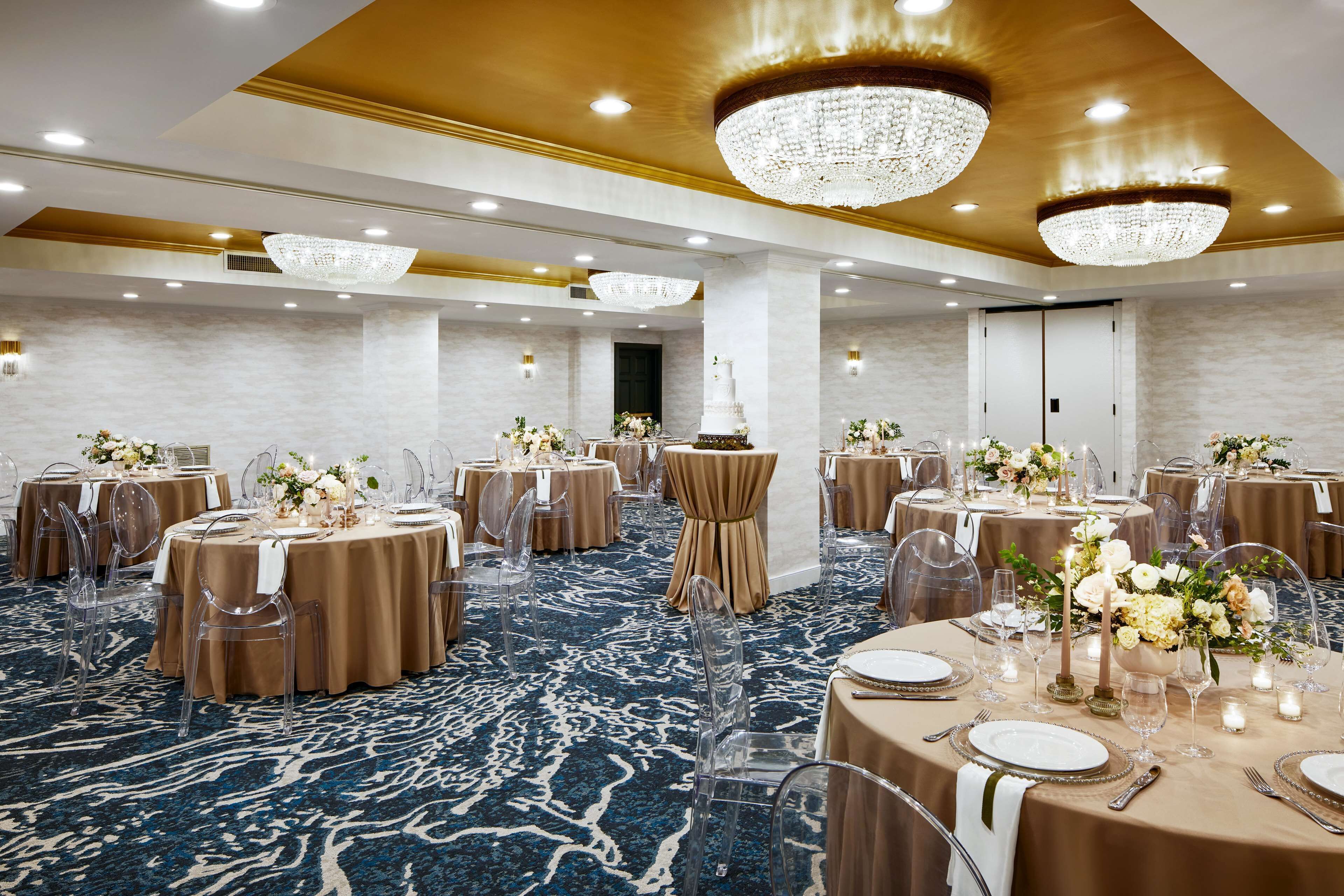Un salón de banquetes con mesas redondas, sillas transparentes y candelabros.