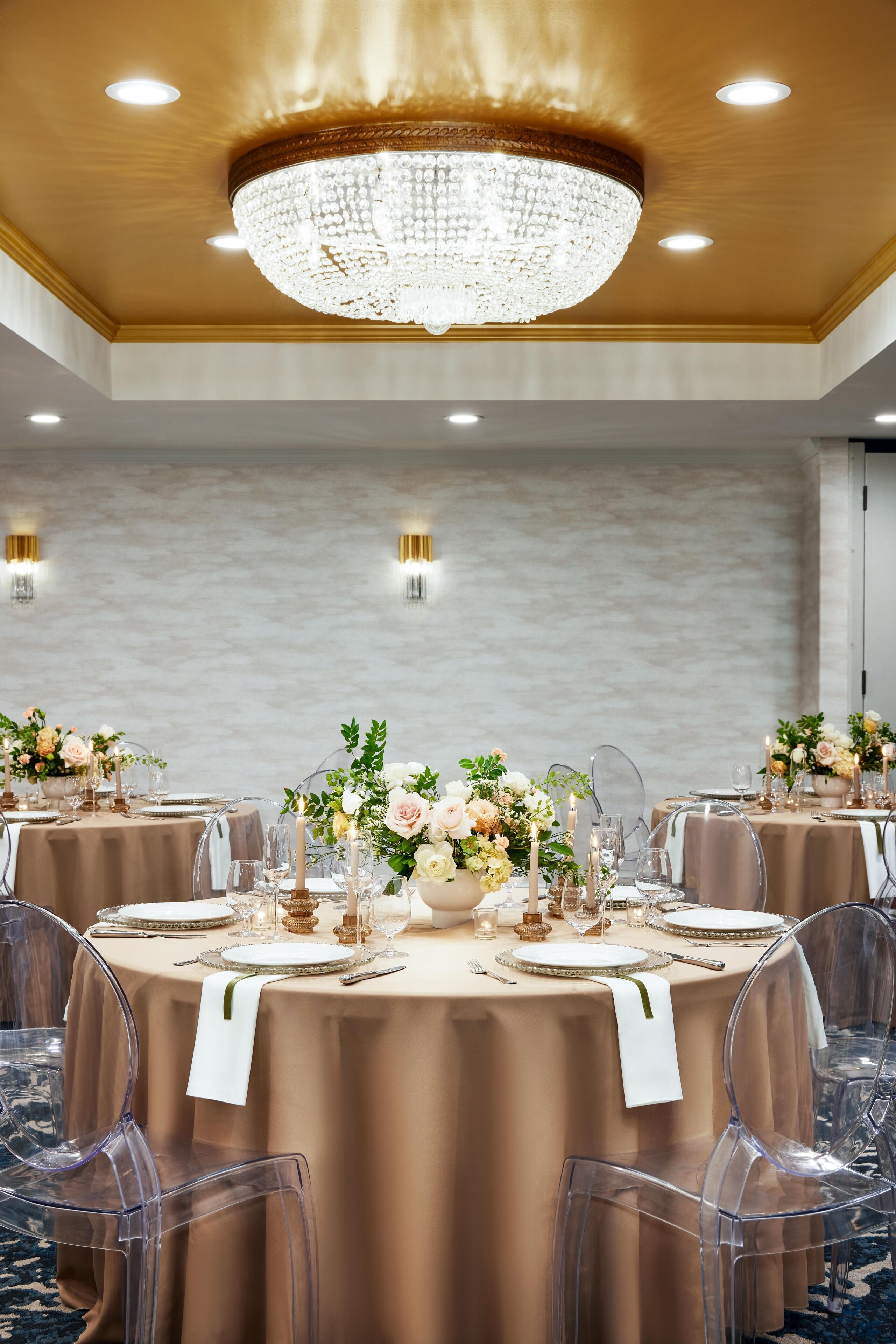 A banquet hall with round tables, clear chairs, and elegant floral centerpieces.