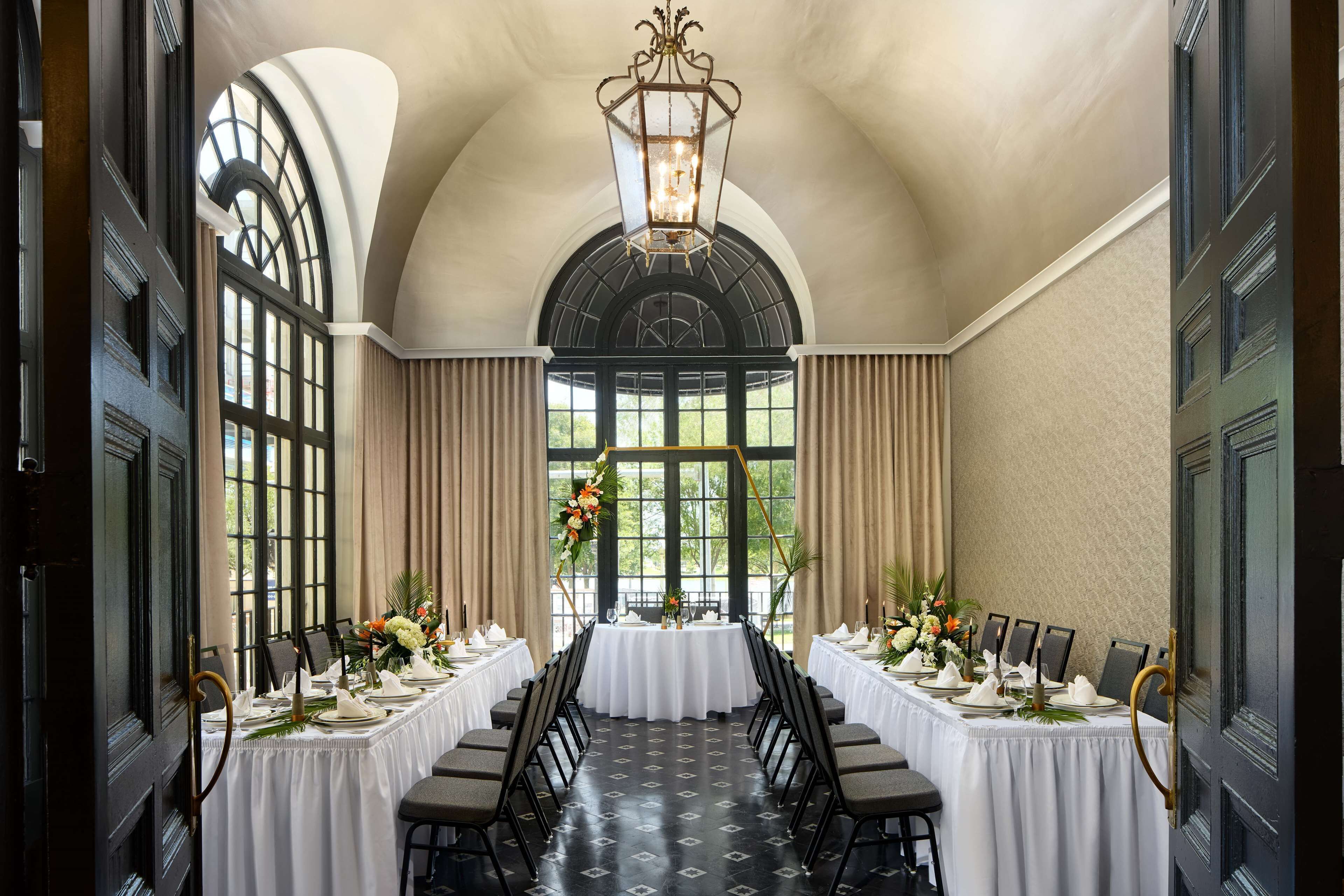 A long dining table set for a formal event, flanked by tall windows and a chandelier.