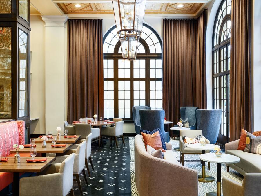 Comedor de hotel con techo alto, ventanas amplias y mobiliario moderno.