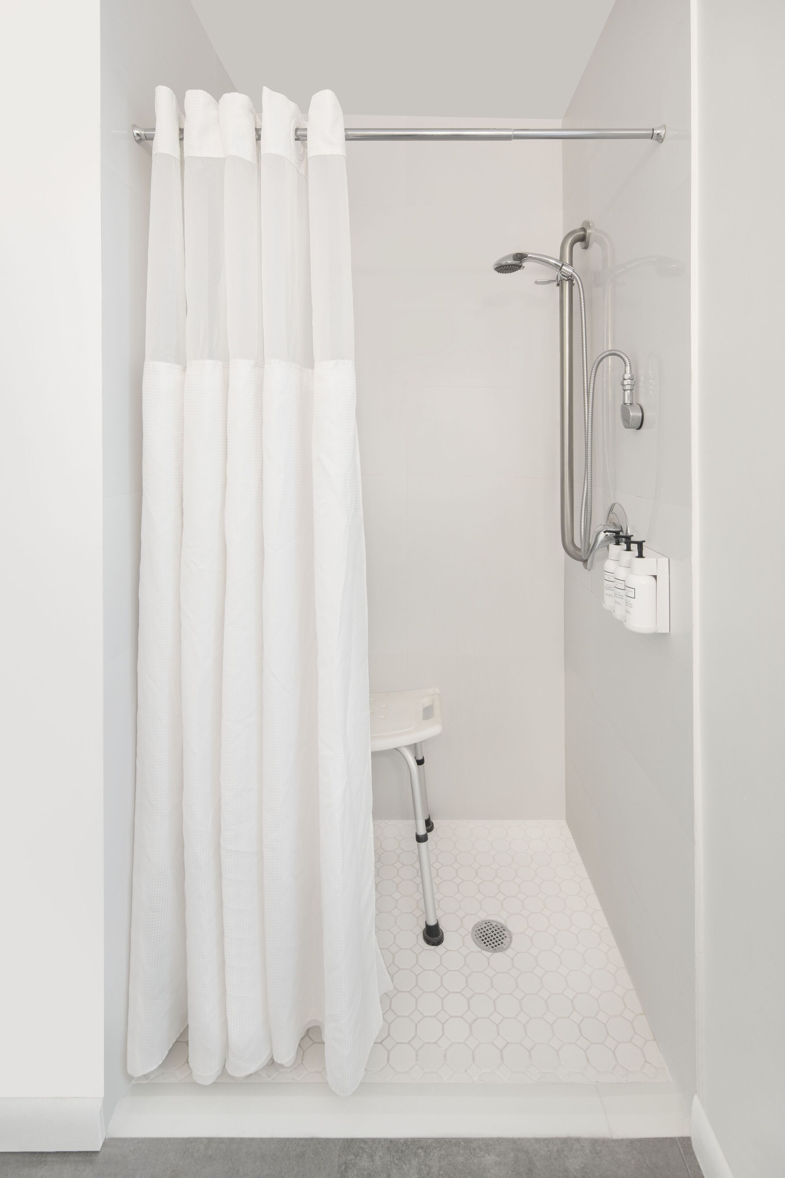 A modern shower area with a white shower curtain, a handheld showerhead, and a handheld shower attachment.
