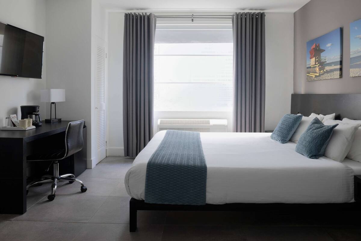 A hotel room with a bed, a desk, a chair, a television, and a window with curtains.