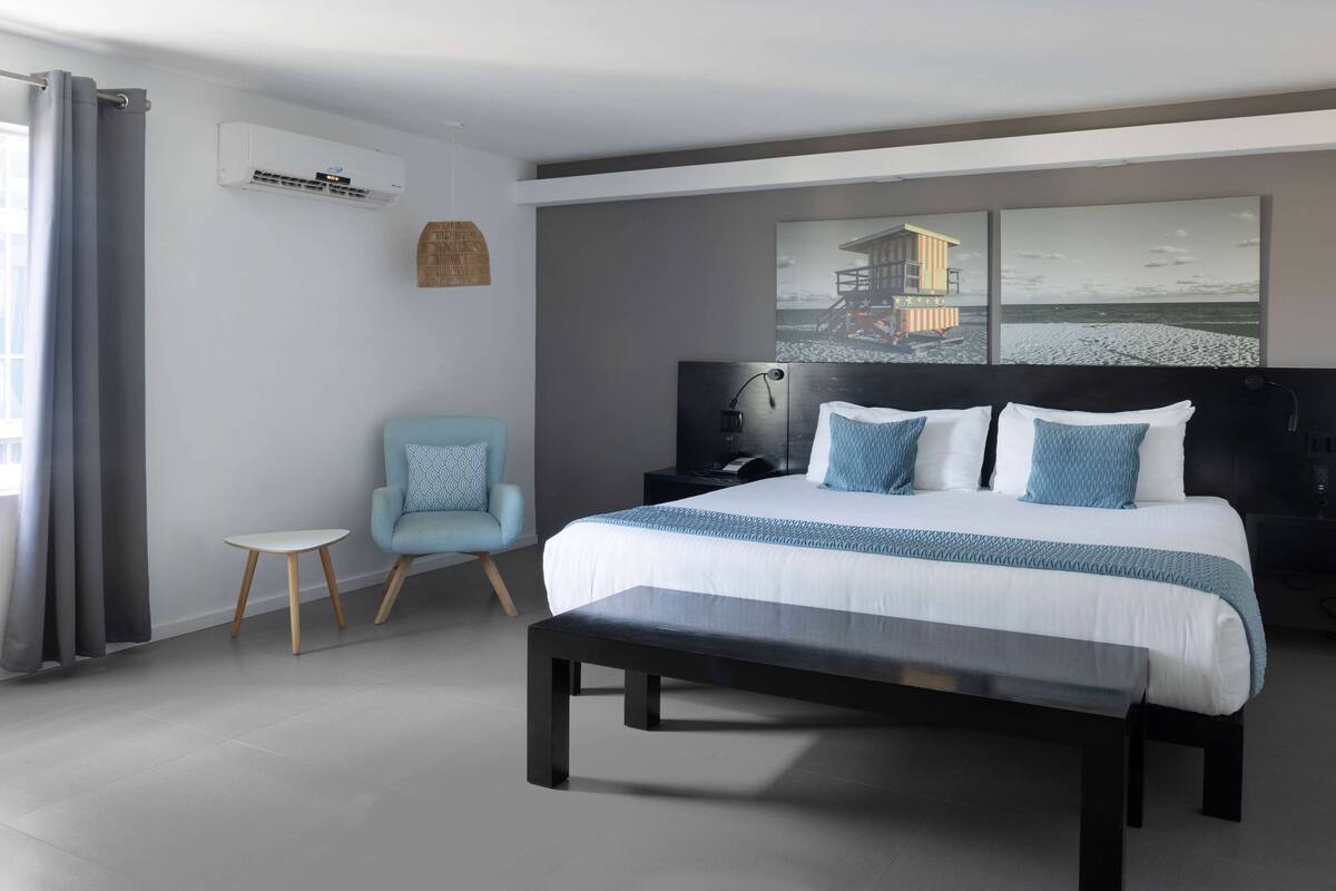 A modern bedroom with a large bed, a bench, a small table, and a chair.