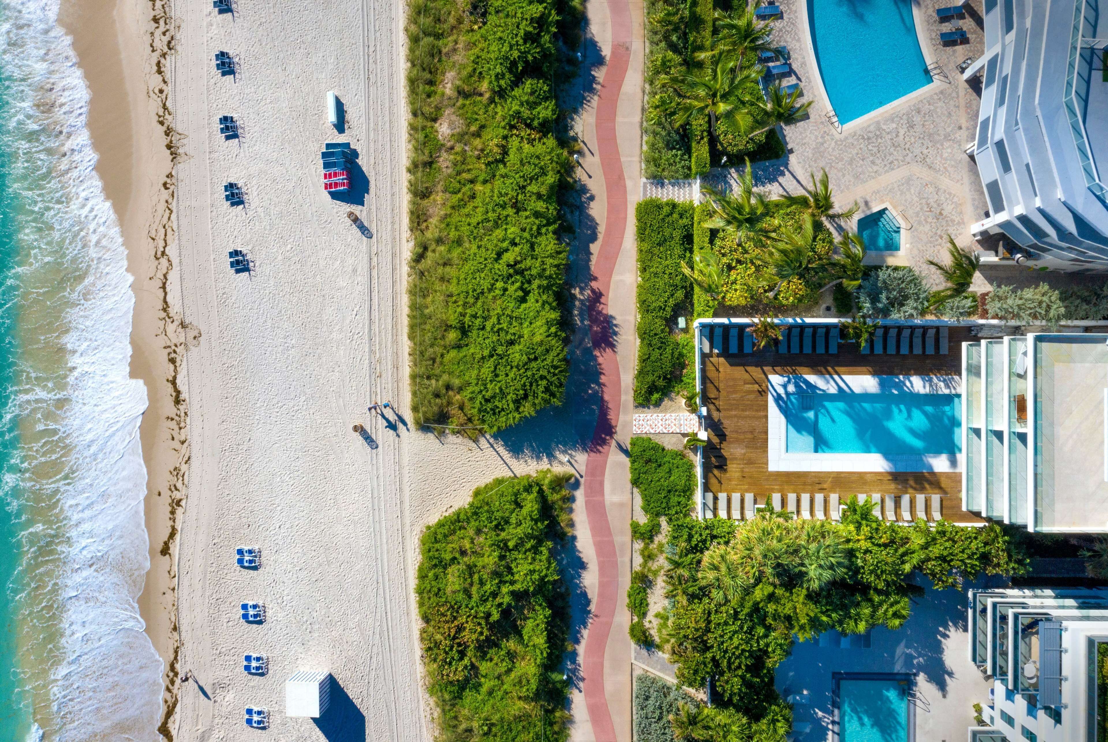 An aerial view of a beachside resort with a swimming pool, beach chairs, and a pathway.