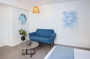 Habitación moderna con un sofá azul, una mesa redonda y una cama. Hay dos obras de arte en las paredes y una planta en maceta.