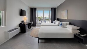 Et moderne hotelværelse med en stor seng, et skrivebord med en computer, et fladskærms-tv og udsigt til en parkeringsplads gennem en skydedør.