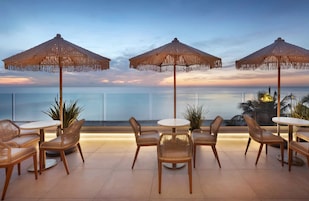 Una terraza con mobiliario de mimbre y sombrillas de paja que da a un mar tranquilo.