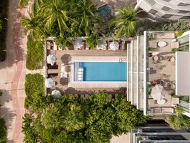 An aerial view of a resort with a swimming pool, lounge area, and palm trees.