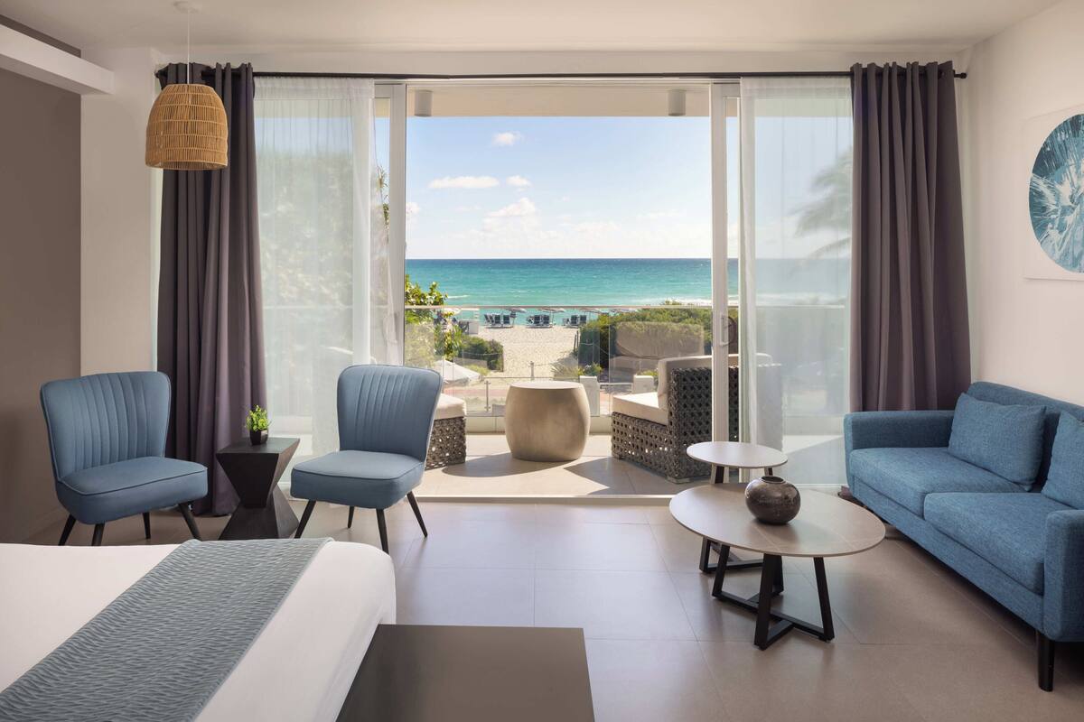 A hotel room with a balcony, a bed, two armchairs, a sofa, and a small table.