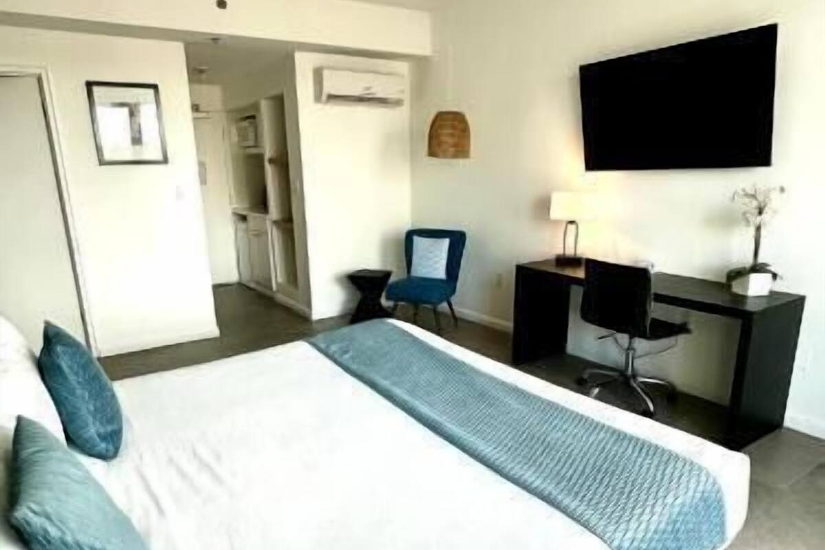 A hotel room with a bed, a desk with a computer, a chair, and a television on the wall.