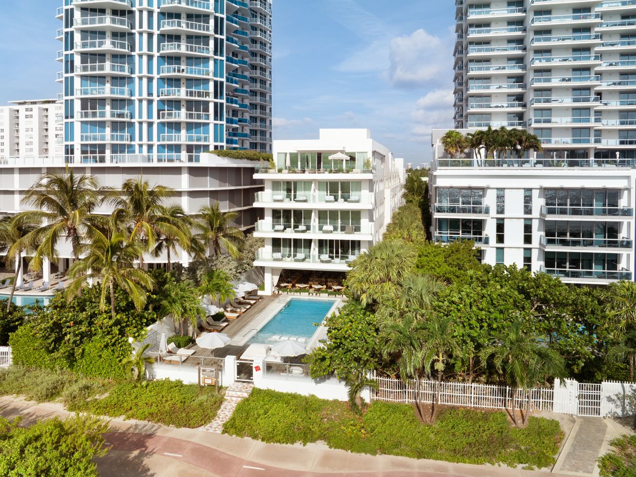 Hotel moderno com piscina, cercado por palmeiras e vegetação.