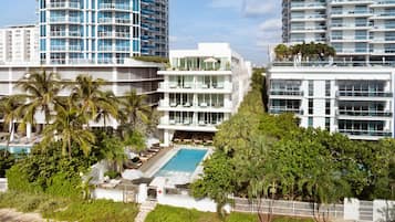Hotel moderno com piscina, cercado por palmeiras e vegetação.