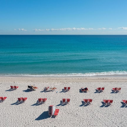 A beach with rows of red and white sun loungers facing the ocean.