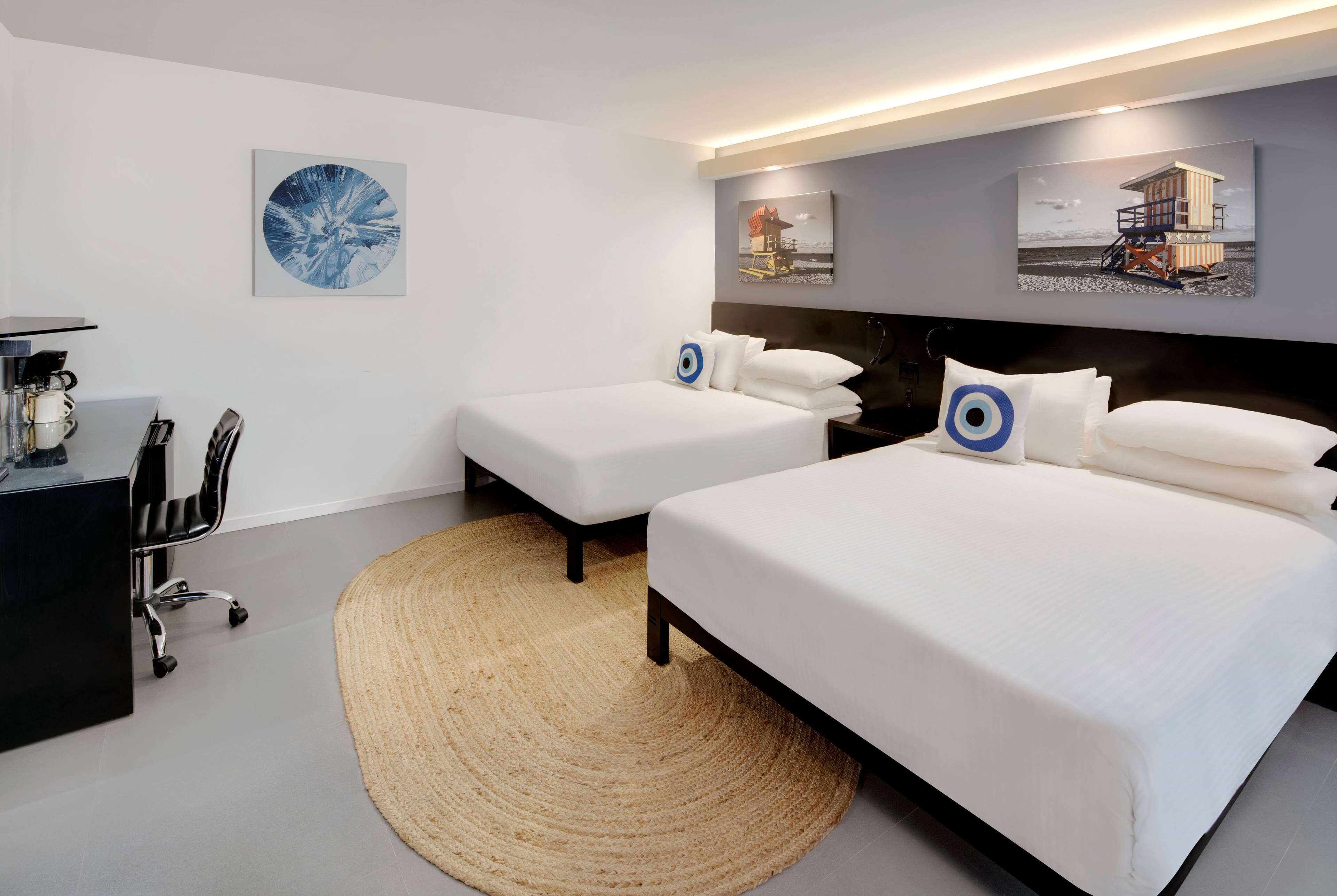 Une chambre d’hôtel avec deux lits simples, un bureau avec une chaise et un grand tapis tissé.