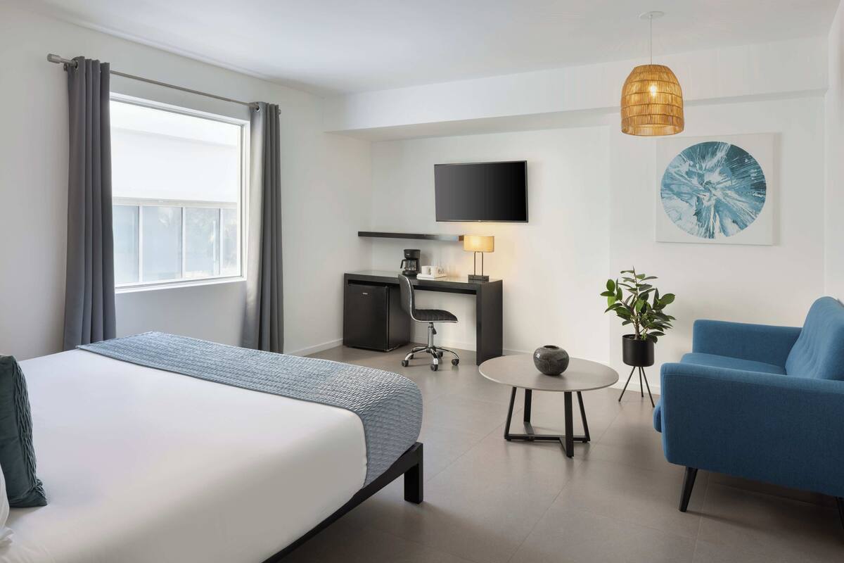A hotel room with a bed, desk, chair, lamp, and artwork.
