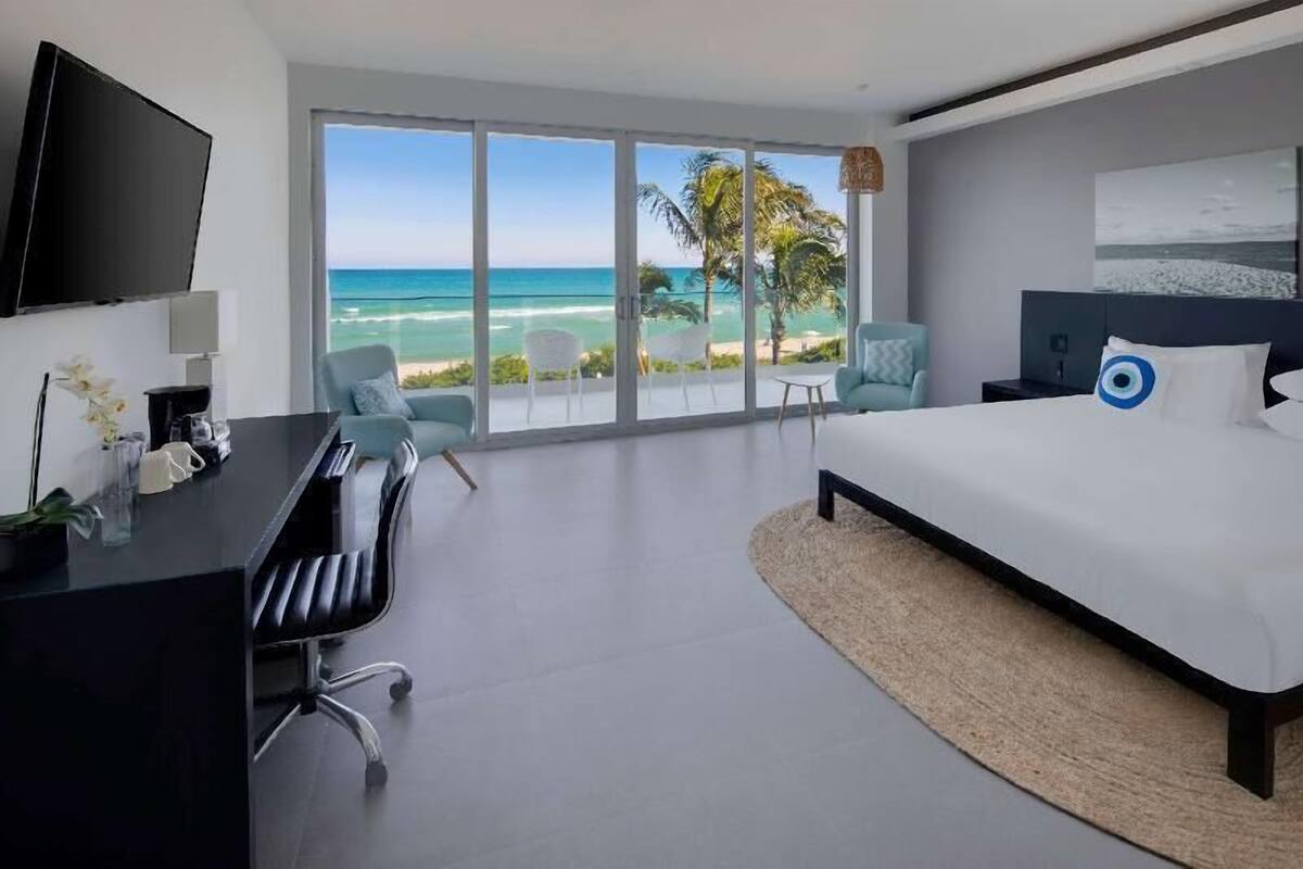 A modern hotel room with a large bed, a desk, a chair, and a TV.
