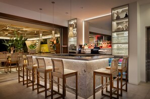 A modern bar area with a marble counter, wicker chairs, and a variety of bottles and glasses. - MB Hotel, Trademark Collection by Wyndham (Miami Beach)