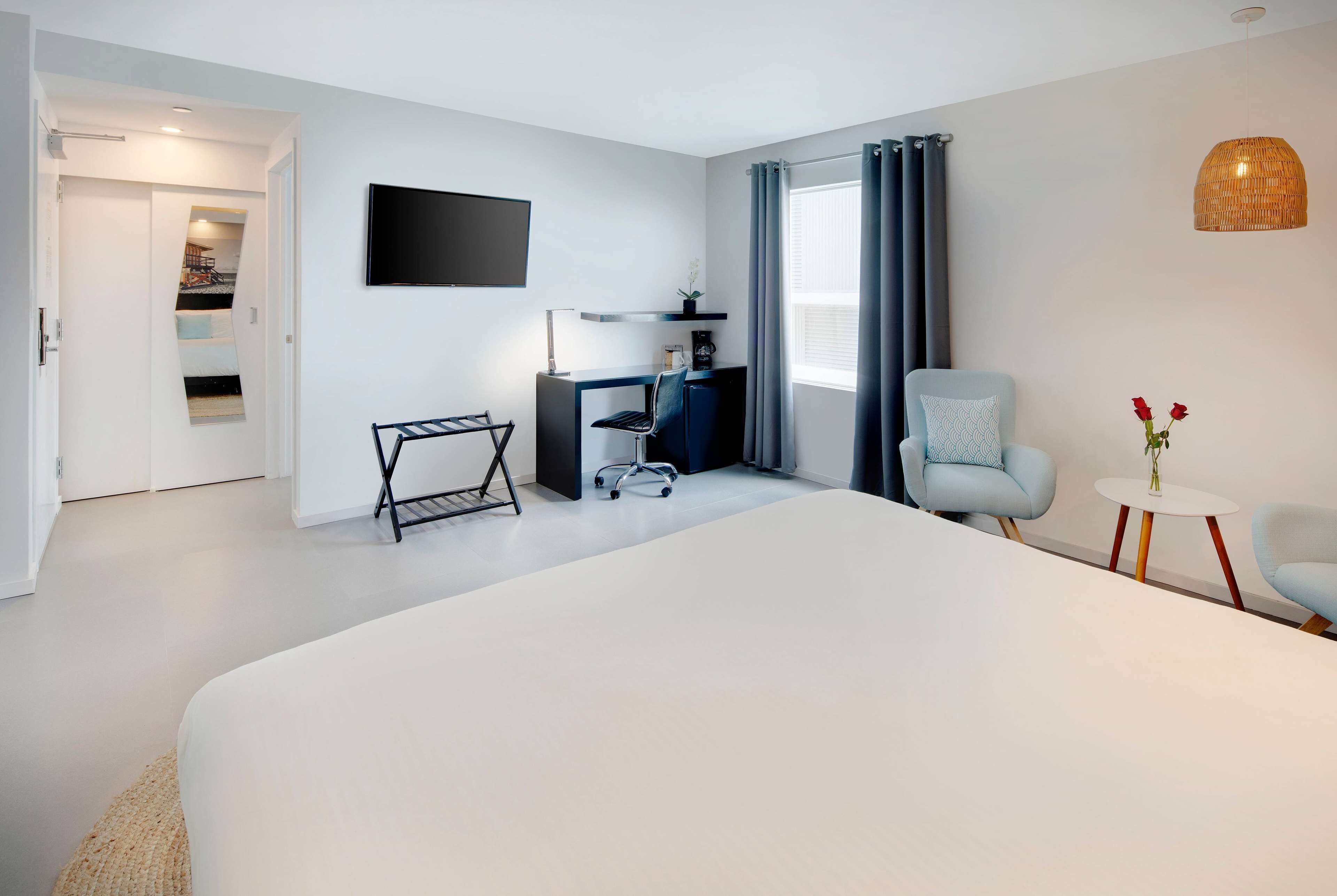 Una habitación de hotel moderna con una cama grande, un escritorio con una silla, un televisor y una pequeña mesa con flores.
