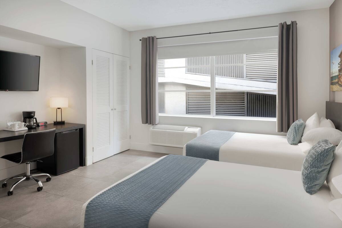 A hotel room with a bed, a desk, a chair, a TV, and a window with curtains.