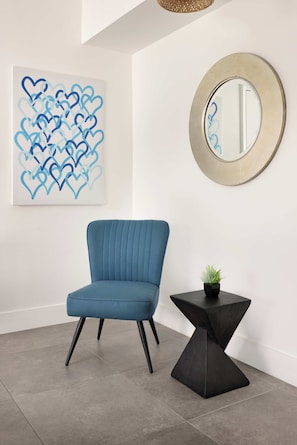 Una habitación moderna con un sillón azul, un espejo redondo y una obra de arte en la pared.