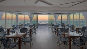 En restaurant med udsigt over havet i solnedgang, med borde og stole arrangeret til spisning.
