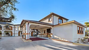 Ein zweistöckiges Haus mit überdachter Terrasse, rotem Teppich und kleinem Garten.