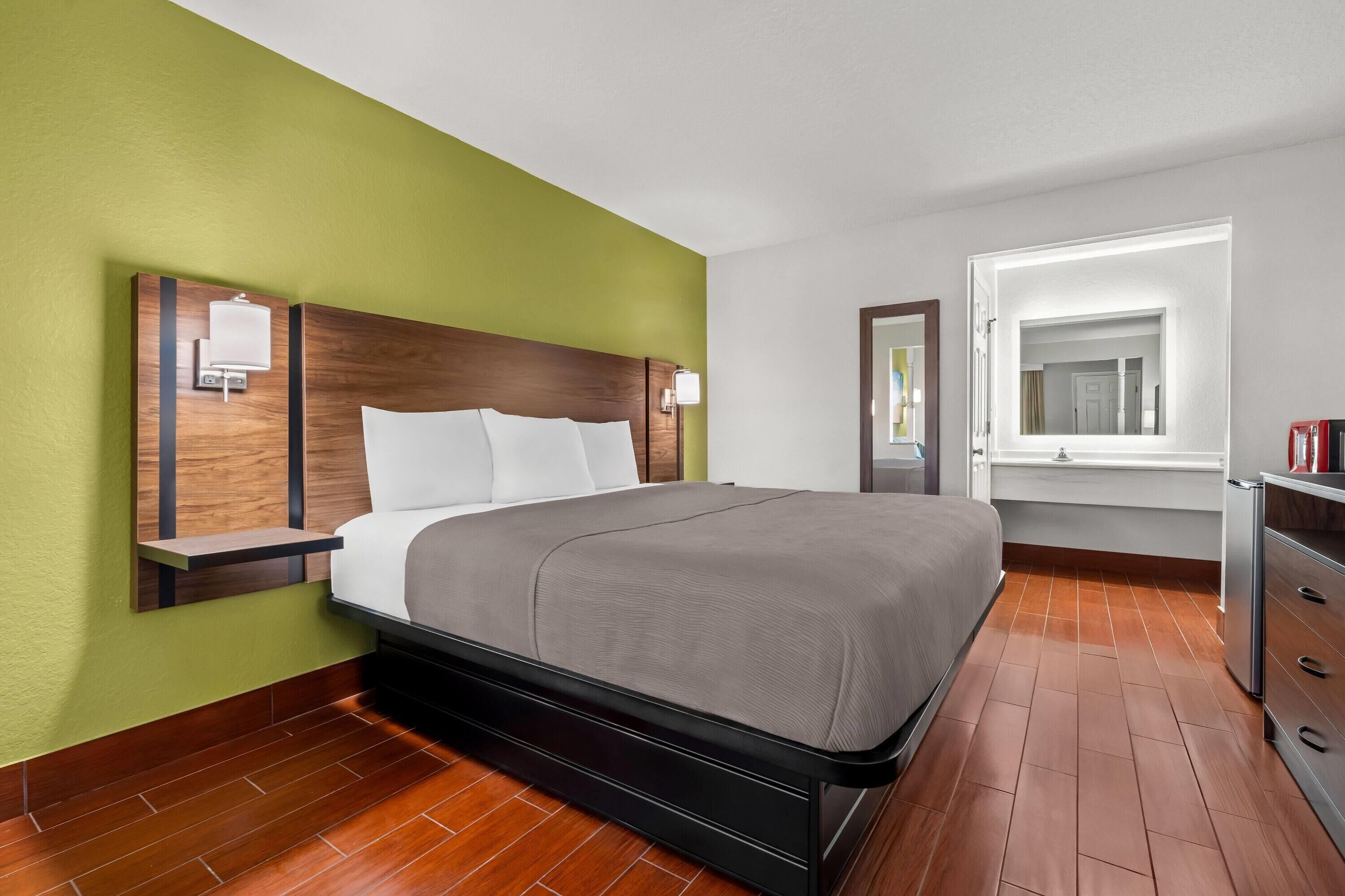 A hotel room with a bed, a nightstand, a dresser, and a window with a view.