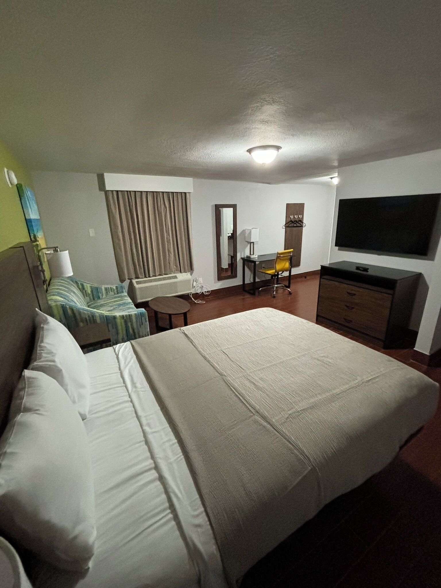 A hotel room with a large bed, a desk with a chair, a television, and a mirror.