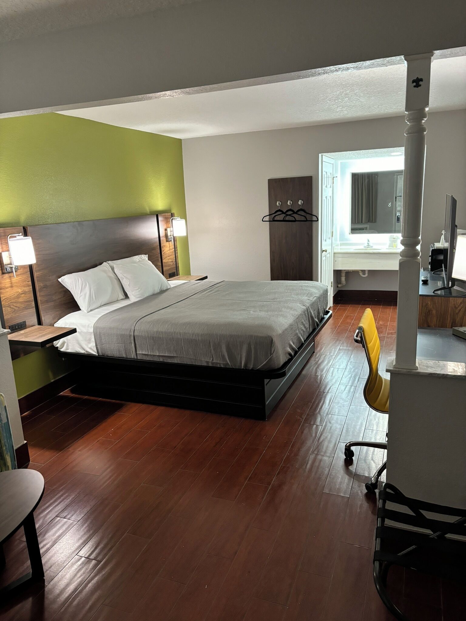 Une chambre d’hôtel moderne avec un grand lit, un bureau avec une chaise, une armoire et une salle de bain visible à travers une porte ouverte.