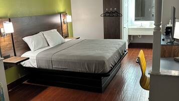 Une chambre d’hôtel moderne avec un grand lit, un bureau avec une chaise, une armoire et une salle de bain visible à travers une porte ouverte.
