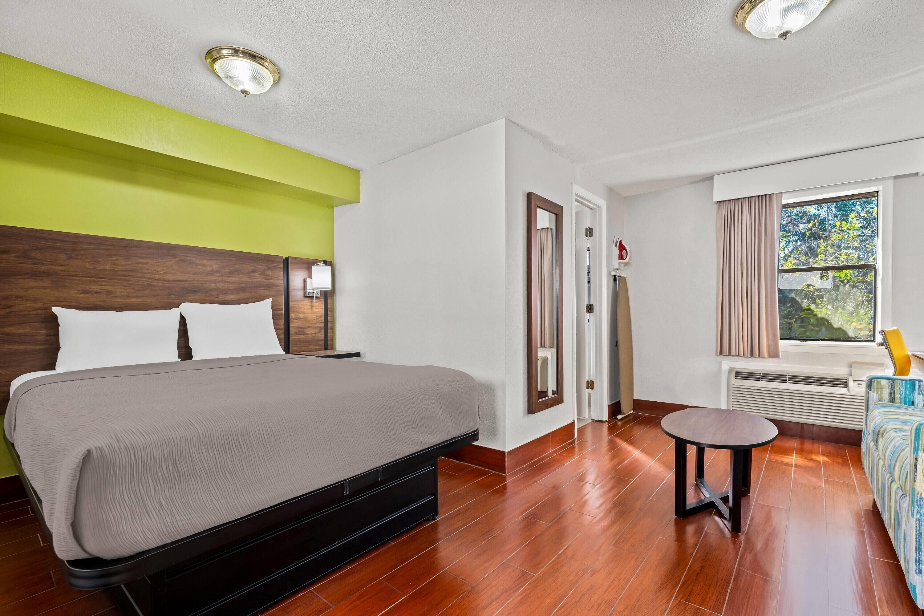 Quarto de hotel com uma cama grande, uma mesa pequena redonda, uma janela com cortinas e um radiador.