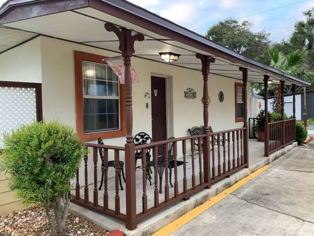 A building with a covered porch, a small tree, and a few chairs.