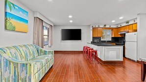 Una sala de estar moderna con un sofá, un televisor de pantalla plana y una cocina con armarios de madera y un refrigerador.