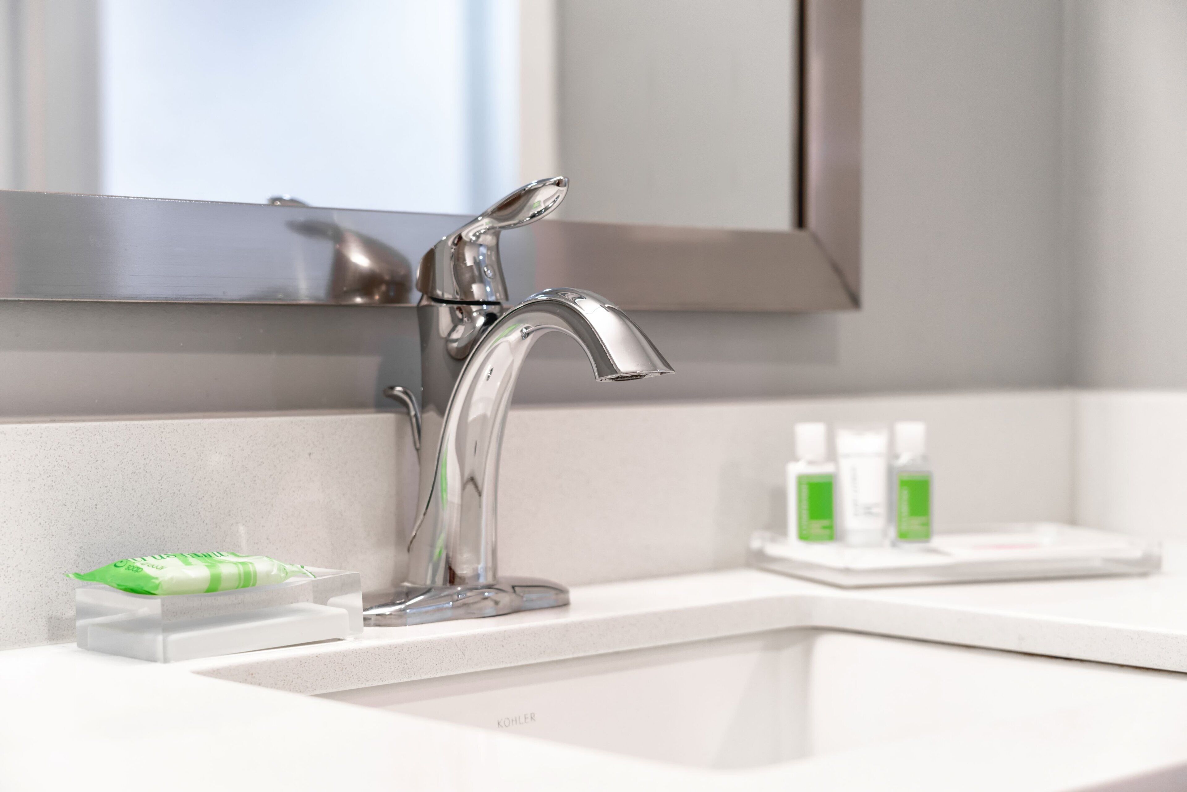 A modern bathroom with a chrome faucet, a mirror, and a small shelf with toiletries.