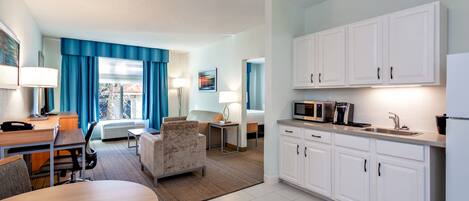 Una habitación de hotel moderna con comedor, kitchenette y un amplio ventanal con cortinas azules.