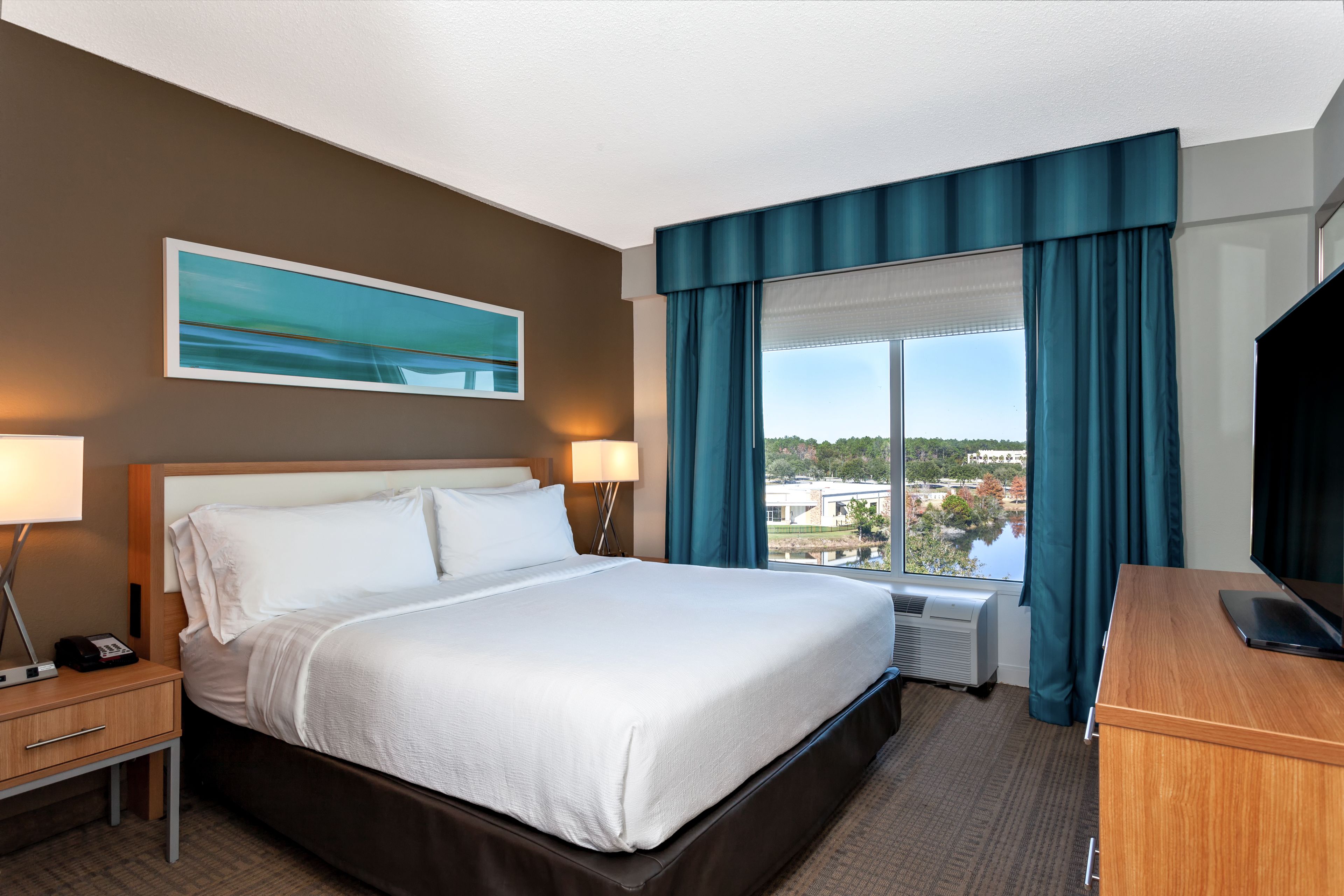 Een hotelkamer met een groot bed, een bureau, een televisie en een raam met gordijnen.