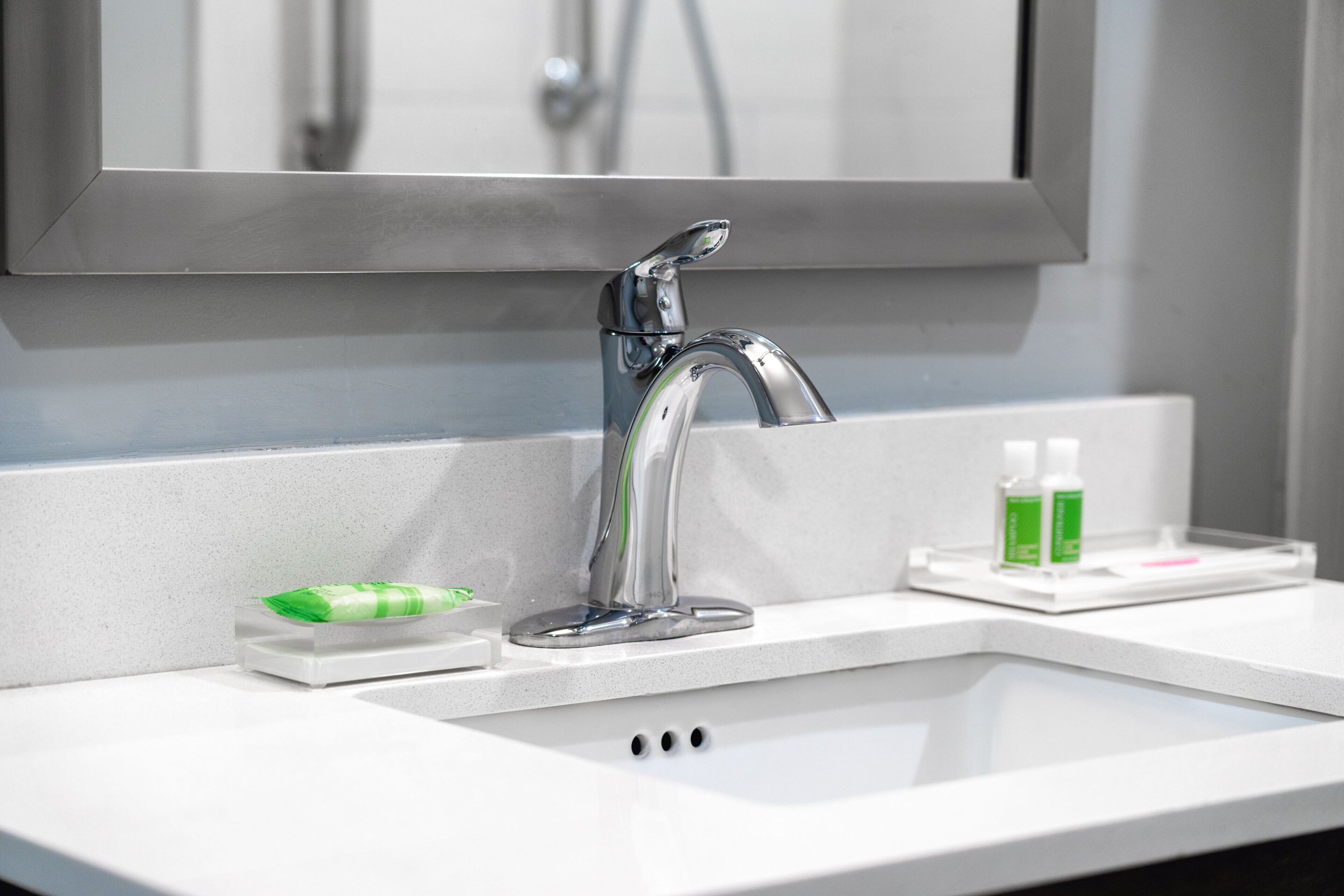 A modern bathroom with a chrome faucet, a mirror, and a soap dispenser on the counter.
