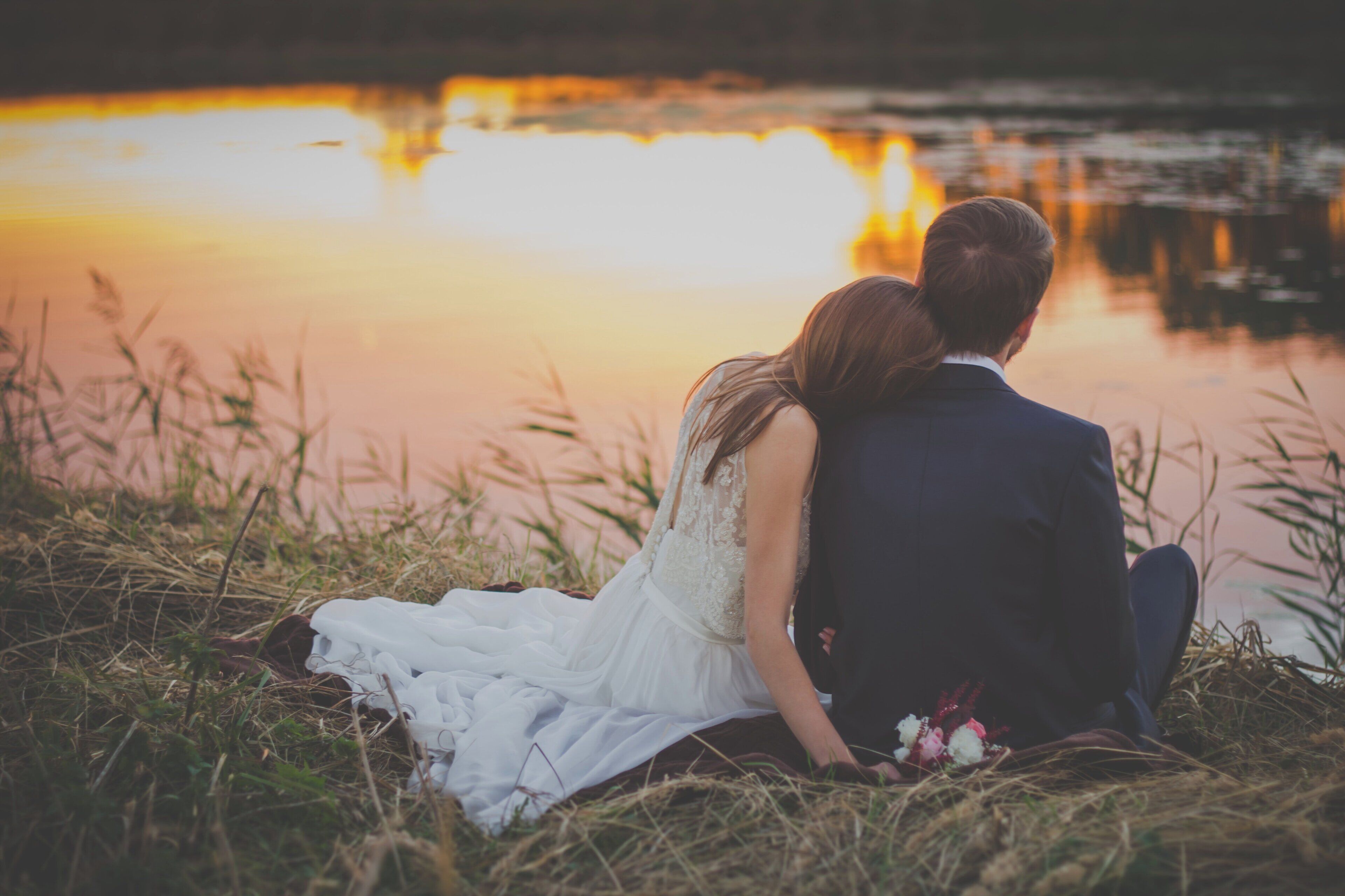 A couple sitting by a body of water during sunset.