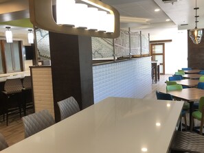 A modern restaurant interior with a long white table, blue-tiled counter, and colorful chairs.