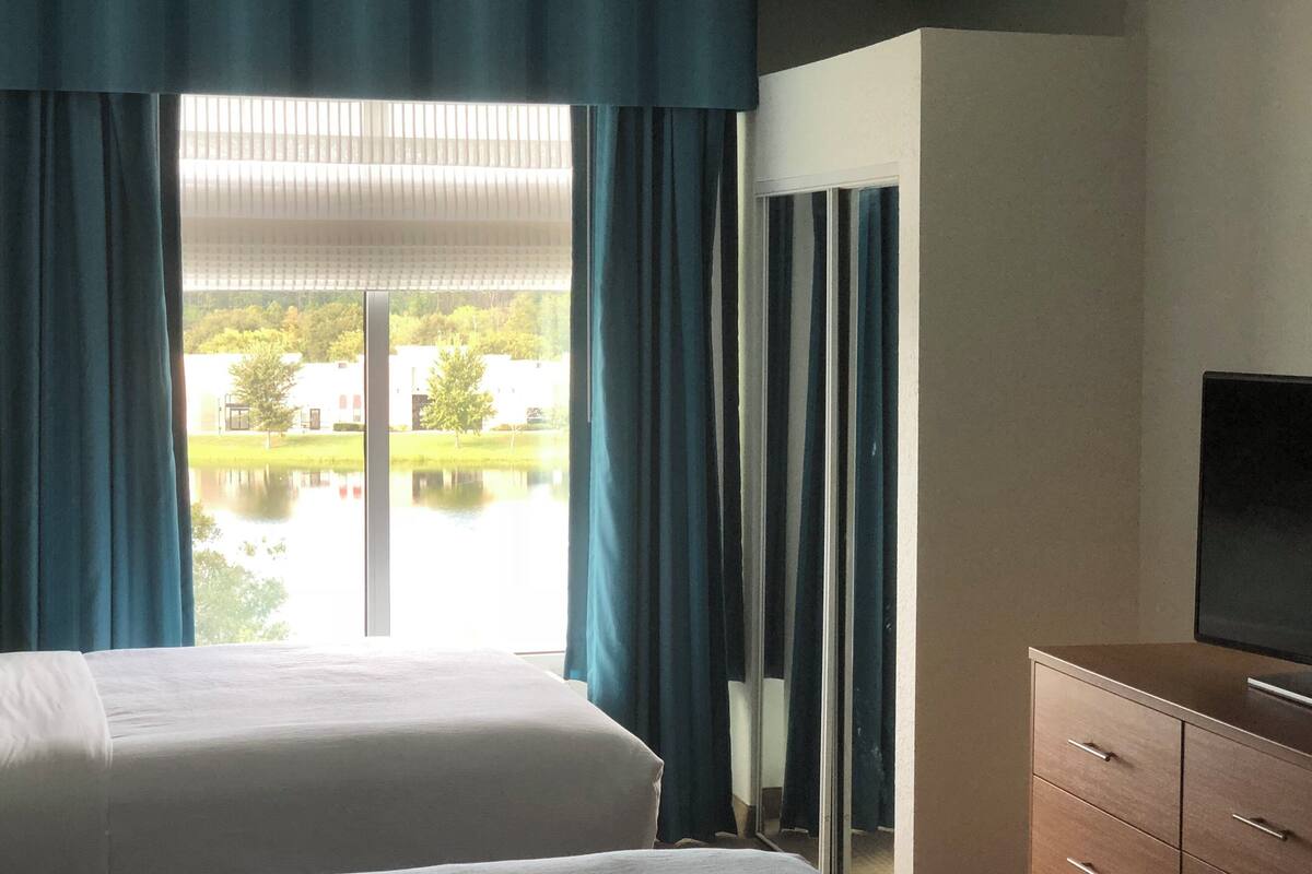 Une chambre d’hôtel avec deux lits, une télévision et une vue sur un lac et des bâtiments.