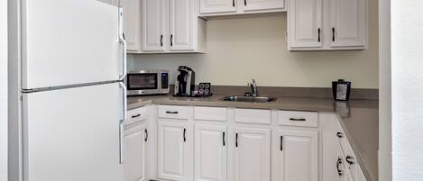 A kitchen with white cabinets, a refrigerator, a microwave, a coffee maker, and a sink.