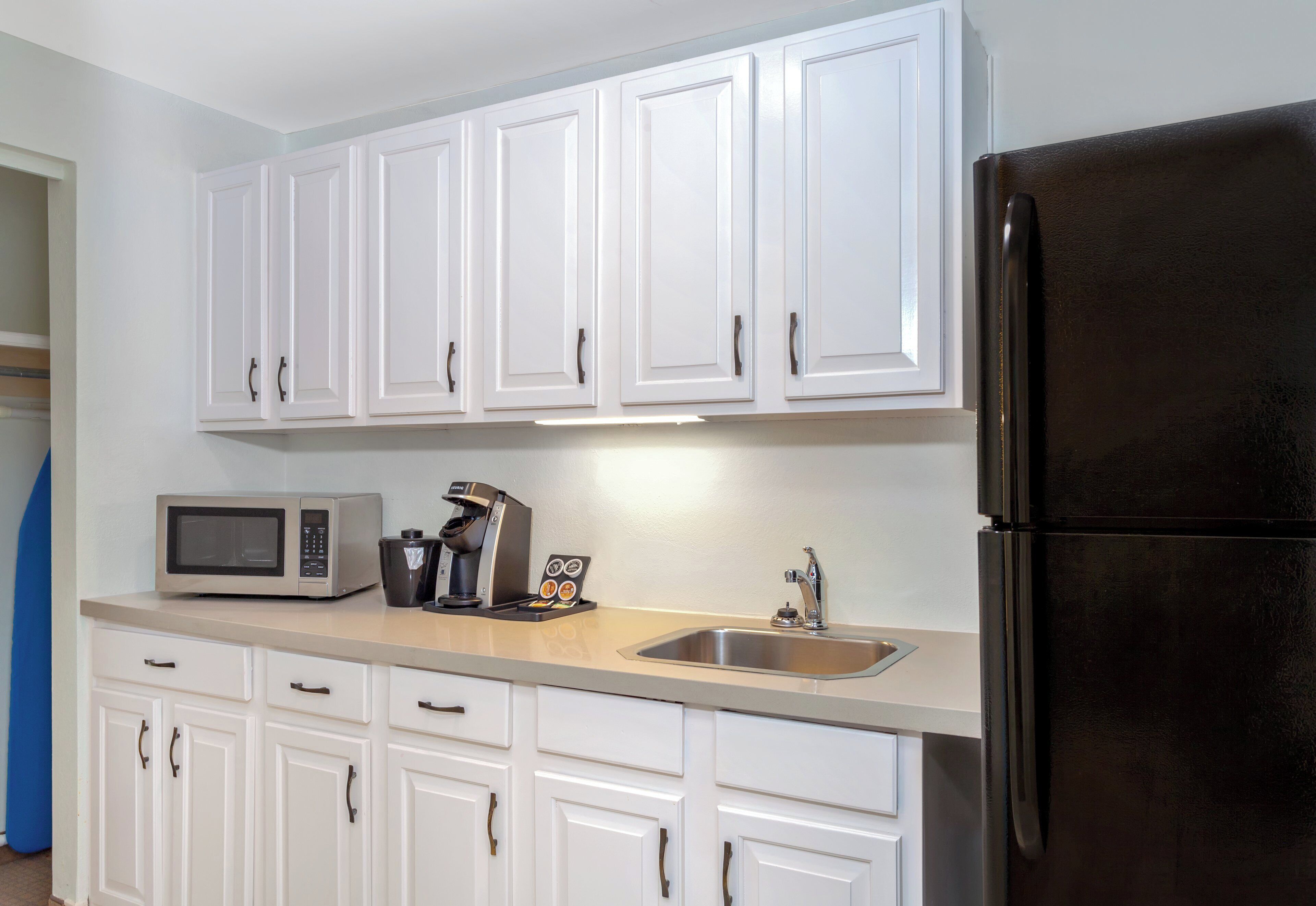A kitchen with white cabinets, a stainless steel refrigerator, a microwave, and a coffee maker.