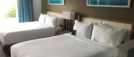 Una habitación de hotel con dos camas, una mesita de noche con lámpara y dos cuadros en la pared.