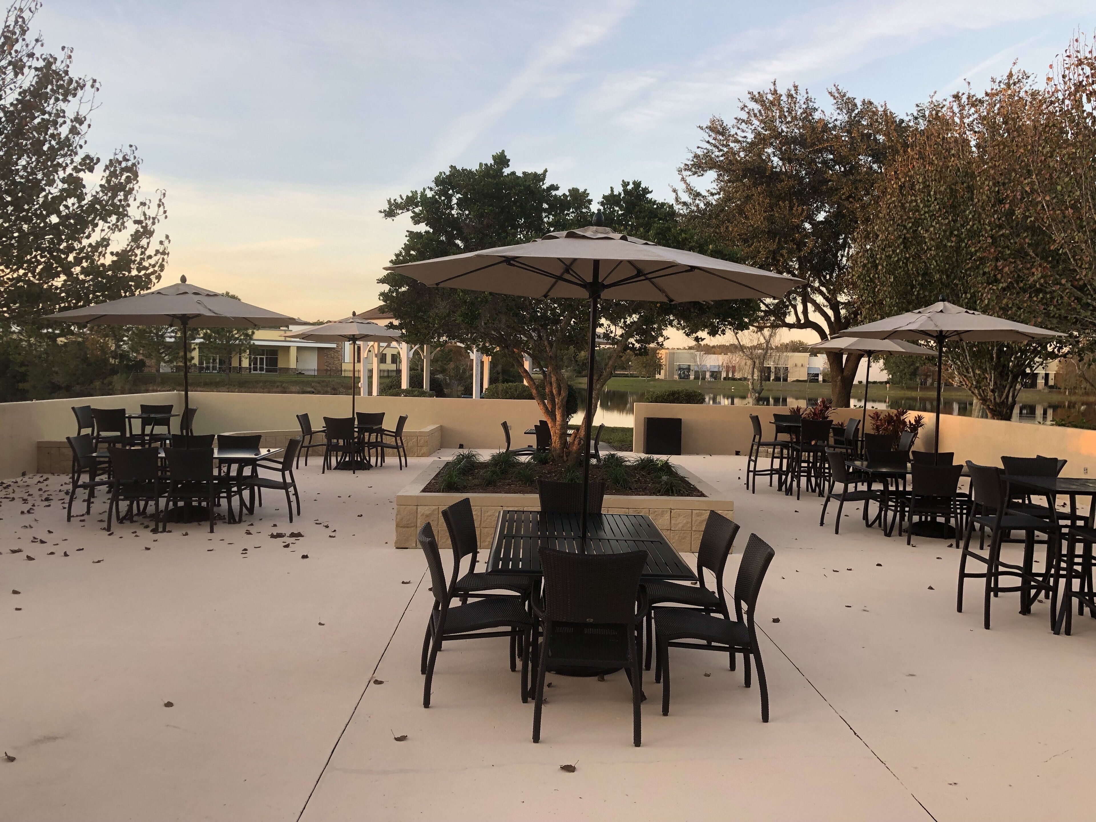 An outdoor patio with tables and chairs, surrounded by trees and a view of a body of water.