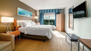 Une chambre d’hôtel comprenant un lit, des tables de chevet, un bureau, une chaise, une télévision et une fenêtre avec des rideaux.