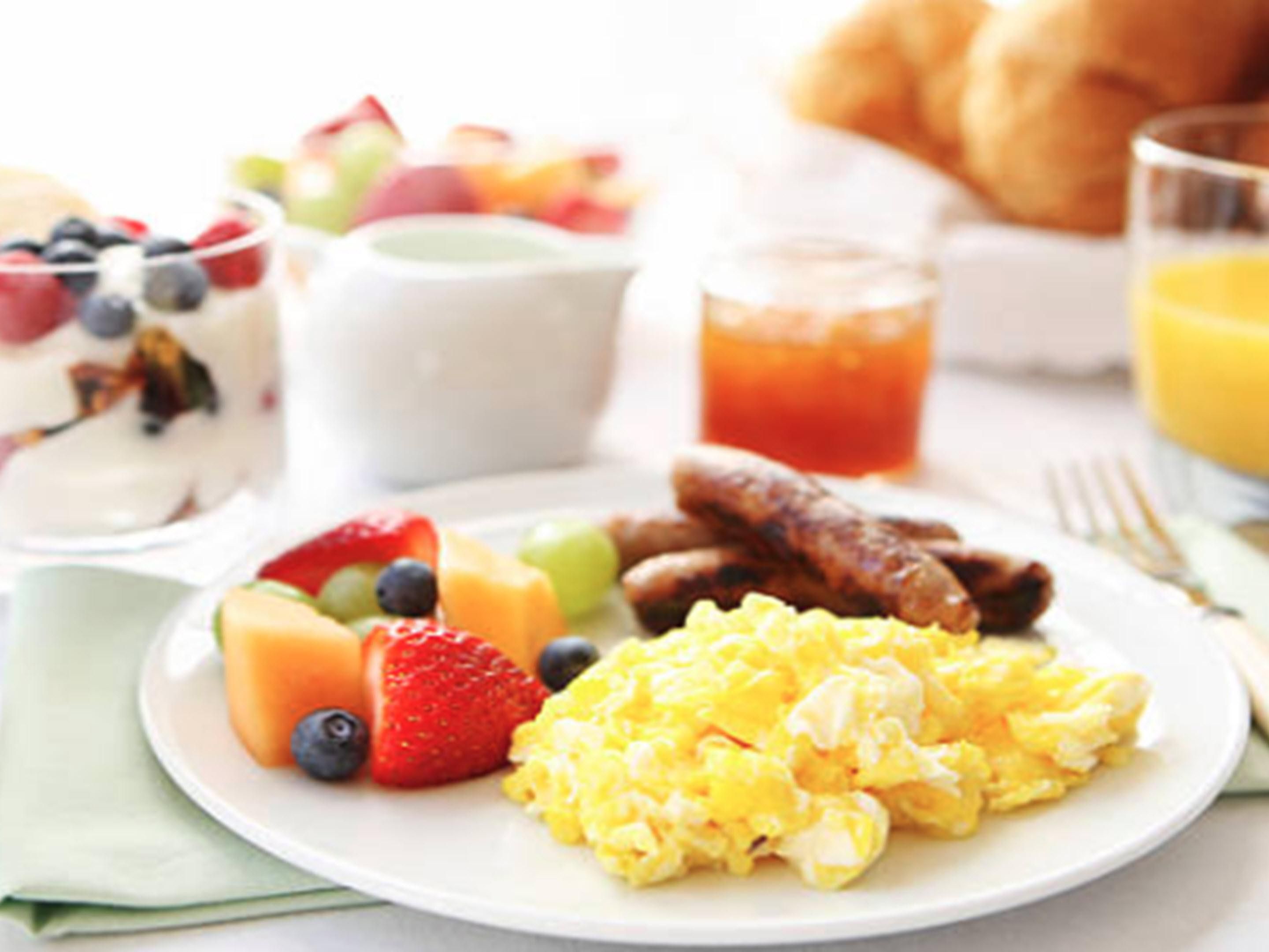A breakfast plate with scrambled eggs, sausages, strawberries, blueberries, and a glass of orange juice.