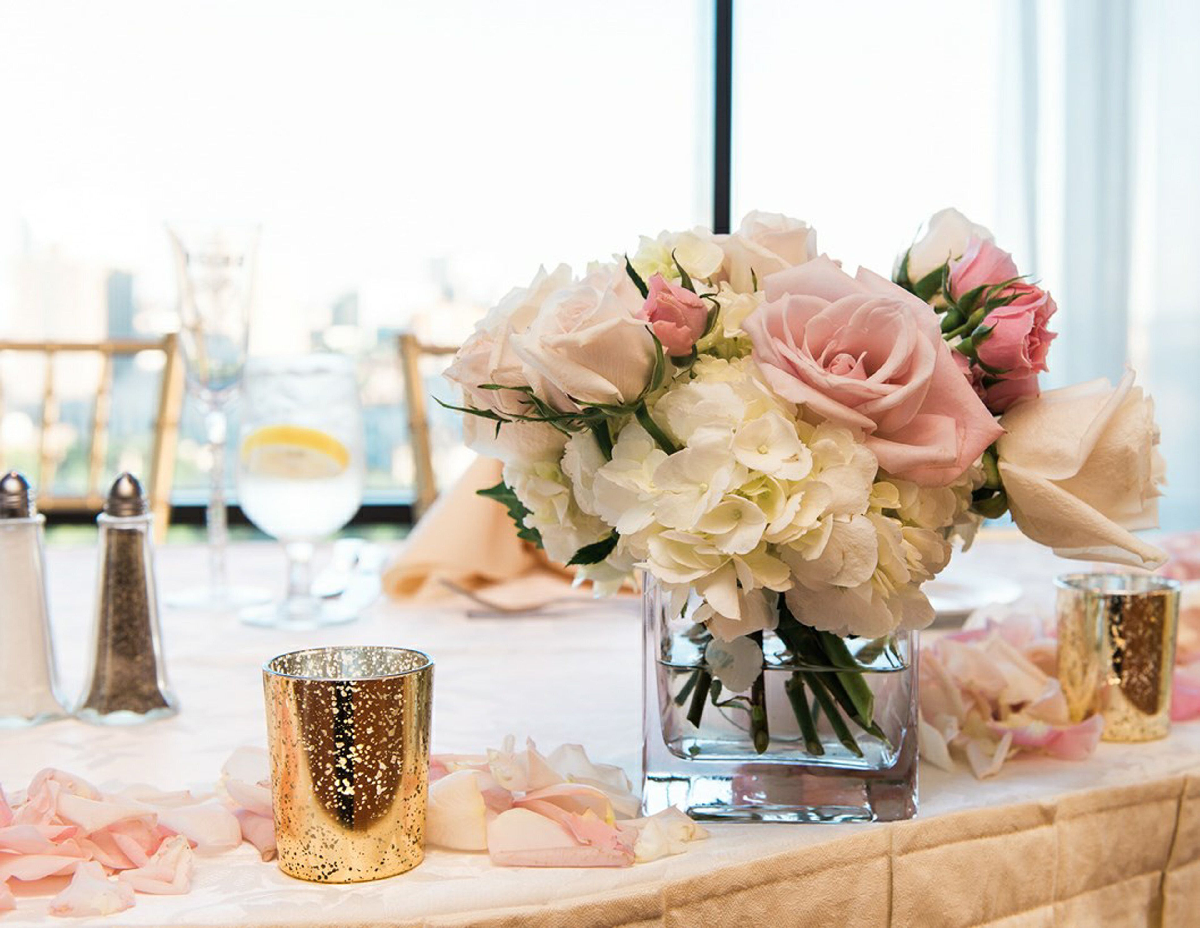 A table set with a vase of flowers, a gold candle holder, and a glass candle.